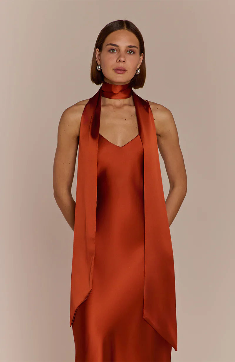 Woman wearing a Burnt Orange  REWRITTEN Brooklyn Bridesmaid Dress with a matching scarf against a beige background