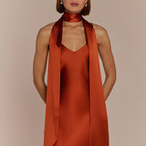 Woman wearing a Burnt Orange  REWRITTEN Brooklyn Bridesmaid Dress with a matching scarf against a beige background
