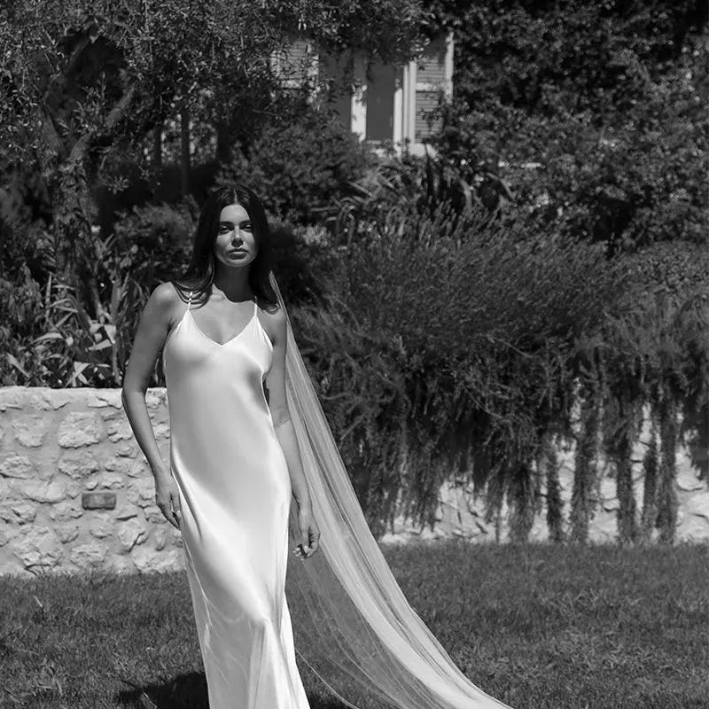 Bride in an ivory silk slip wedding dress with a long veil in a sunlit garden, available to rent at Something Borrowed