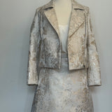 Elegant women's two-piece jacquard outfit on a dress mannequin, featuring a light cream and silver floral-patterned cropped jacket and matching A-line skirt, styled with a soft satin camisole underneath against a plain background.