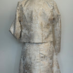 Back of an elegant women's two-piece jacquard outfit on a dress mannequin, featuring a light cream and silver floral-patterned 