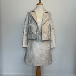 Elegant women's two-piece jacquard outfit on a dress mannequin, featuring a light cream and silver floral-patterned cropped jacket and matching A-line skirt, styled with a soft satin camisole underneath against a plain background.