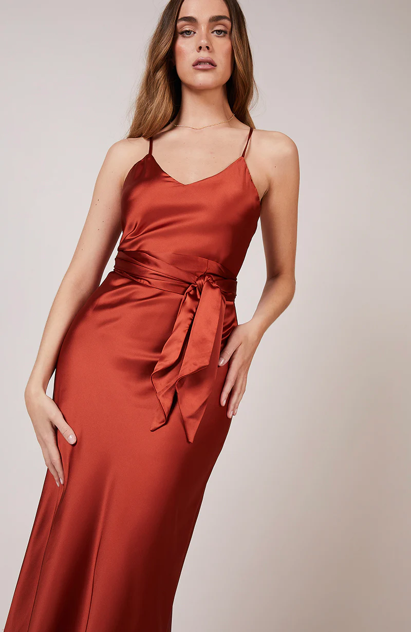A studio photo of a brunette white woman wearing a flowy, rustic-colored satin dress.