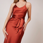 A studio photo of a brunette white woman wearing a flowy, rustic-colored satin dress.