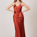 A studio photo of a brunette white woman wearing a flowy, rustic-colored satin dress.