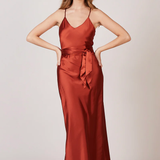 A studio photo of a brunette white woman wearing a flowy, rustic-colored satin dress.