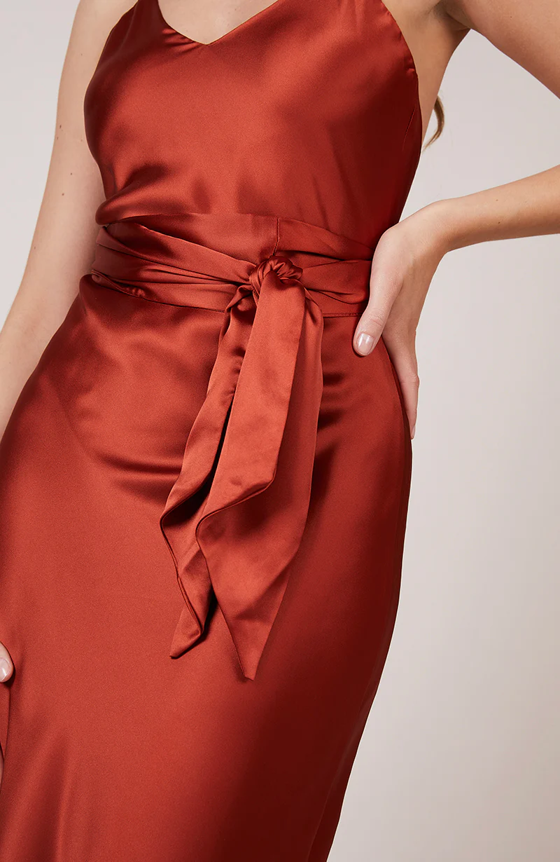A studio photo of a flowy, rustic-colored satin dress.