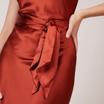A studio photo of a flowy, rustic-colored satin dress.