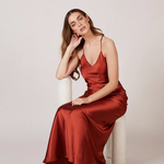 A studio photo of a brunette white woman wearing a flowy, rustic-colored satin dress.