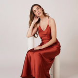 A studio photo of a brunette white woman wearing a flowy, rustic-colored satin dress.
