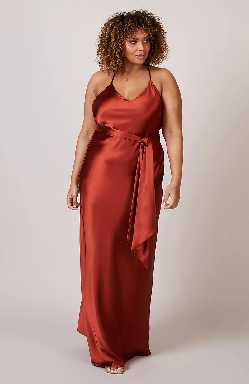 A studio photo of a brunette brown-skinned woman wearing a flowy, rustic-coloured satin dress.