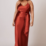 A studio photo of a brunette brown-skinned woman wearing a flowy, rustic-coloured satin dress.