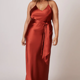 A studio photo of a brunette brown-skinned woman wearing a flowy, rustic-coloured satin dress.