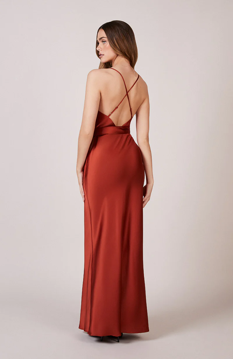 A studio photo of a brunette white woman wearing a flowy, rustic-colored satin dress.
