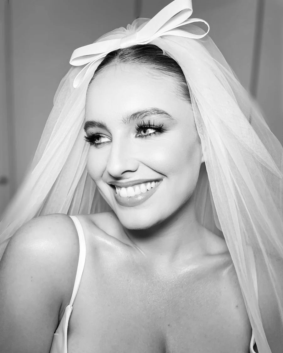 A woman wearing a white elbow-length bridal veil with a flat ivory double bow on top.