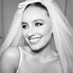 A woman wearing a white elbow-length bridal veil with a flat ivory double bow on top.