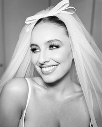 A woman wearing a white elbow-length bridal veil with a flat ivory double bow on top.