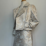 Elegant women's two-piece jacquard outfit on a dress mannequin, featuring a light cream and silver floral-patterned cropped jacket and matching A-line skirt, side styled 
