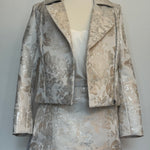 Elegant women's two-piece jacquard outfit on a dress mannequin, featuring a light cream and silver floral-patterned cropped jacket and matching A-line skirt, styled with a soft satin camisole underneath close-view
