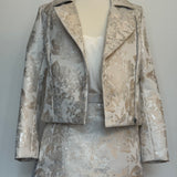 Elegant women's two-piece jacquard outfit on a dress mannequin, featuring a light cream and silver floral-patterned cropped jacket and matching A-line skirt, styled with a soft satin camisole underneath close-view