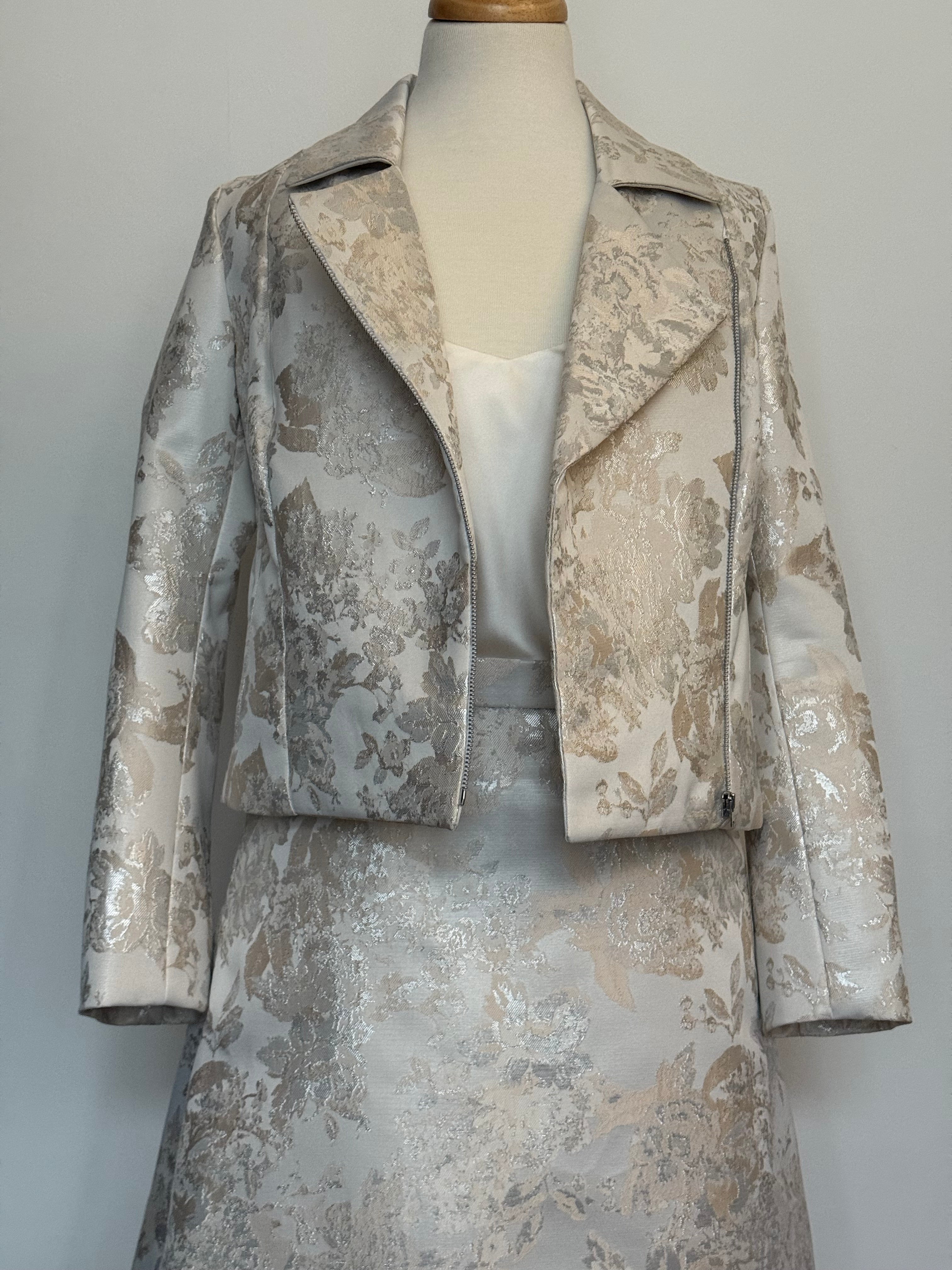 Elegant women's two-piece jacquard outfit on a dress mannequin, featuring a light cream and silver floral-patterned cropped jacket and matching A-line skirt, styled with a soft satin camisole underneath close-view