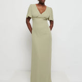 Model in Flattering V-neckline Edie Chiffon Maxi bridesmaid dress in olive green,  under Bust detailing with floaty cap sleeves against a white background