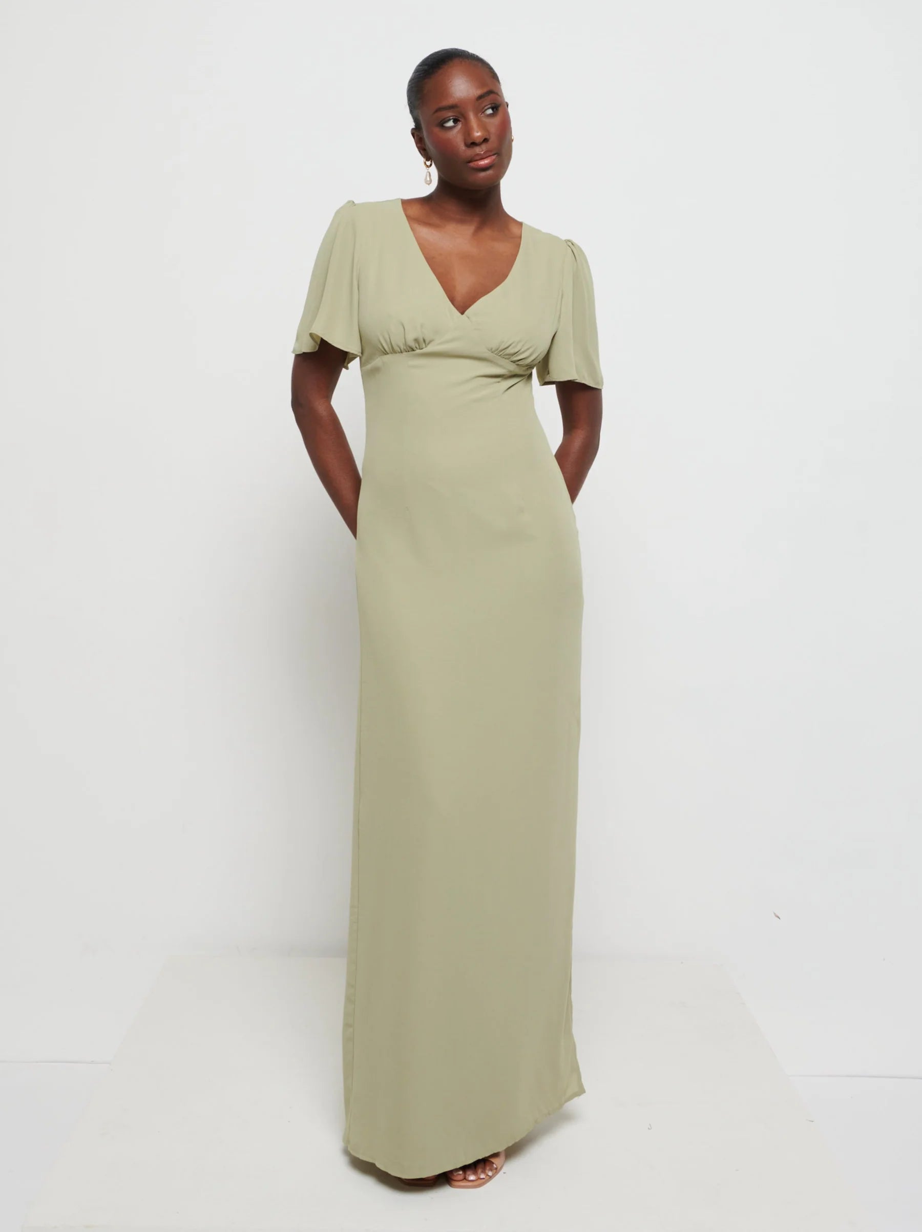 Model in Flattering V-neckline Edie Chiffon Maxi bridesmaid dress in olive green,  under Bust detailing with floaty cap sleeves against a white background