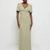 Woman wearing Flattering V-neckline Edie Chiffon Maxi bridesmaid dress in olive green,  under Bust detailing with floaty cap sleeves against a white background