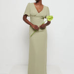 Model in Flattering V-neckline Edie Chiffon Maxi bridesmaid dress in olive green,  under Bust detailing with floaty cap sleeves holding a flower against a white background