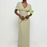 Model in Flattering V-neckline Edie Chiffon Maxi bridesmaid dress in olive green,  under Bust detailing with floaty cap sleeves holding a flower against a white background