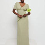 Model in Flattering V-neckline Edie Chiffon Maxi bridesmaid dress in olive green,  under Bust detailing with floaty cap sleeves holding a flower against a white background