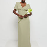 Model in Flattering V-neckline Edie Chiffon Maxi bridesmaid dress in olive green,  under Bust detailing with floaty cap sleeves holding a flower against a white background