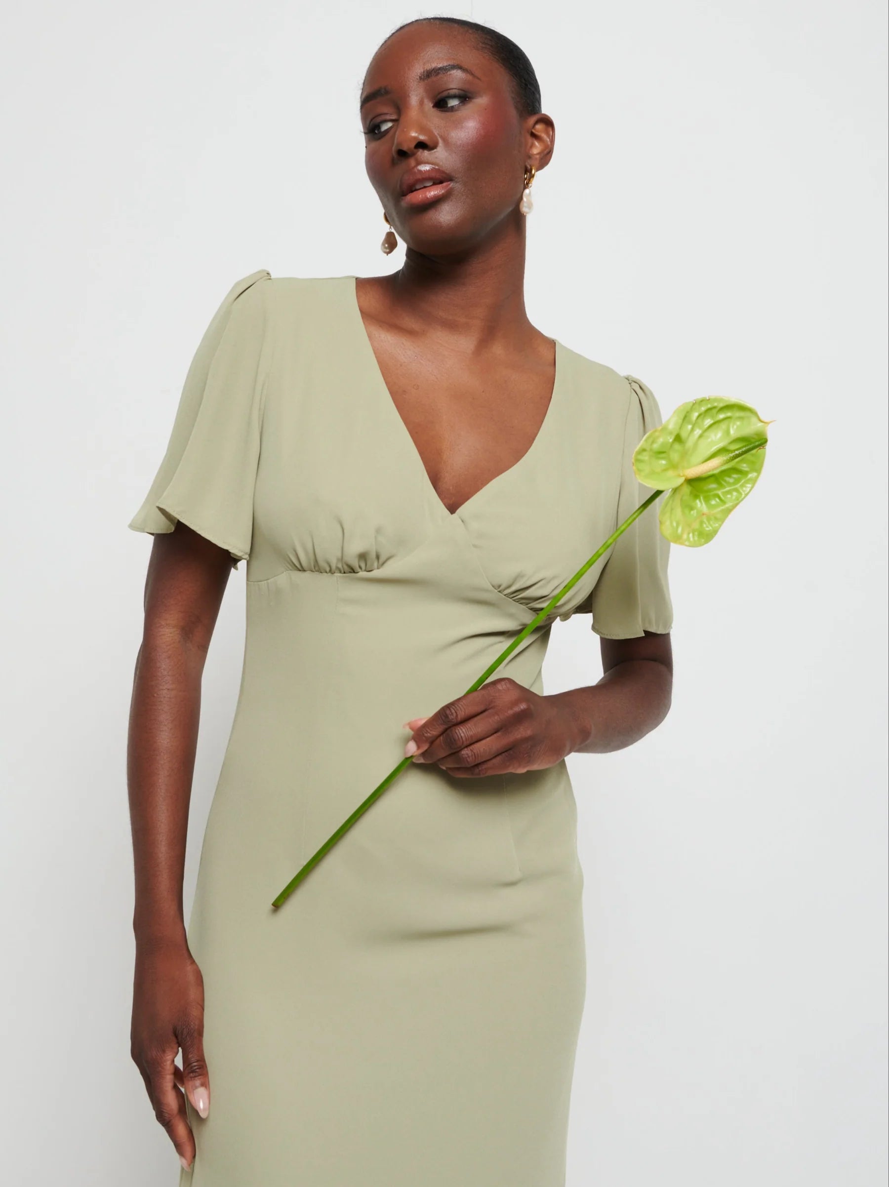 Woman in a  Chiffon Maxi bridesmaid dress holding a green flower against a white background