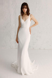 A woman wearing a white OUI THE LABEL Amalfi gown with a square heart neckline and a fluid bias cut skirt.