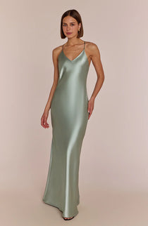 Woman wearing a subtly seductive and effortlessly cool the Brooklyn slip dress  in sage green satin against a beige background