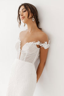 Woman wearing an off-the-shoulder neckline Kismet wedding dress  with  Geometric beaded embroidery .
