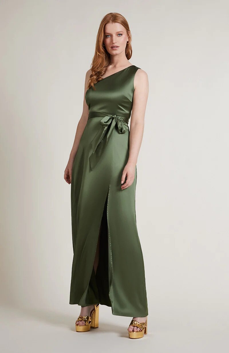A studio photo of a brunette white woman wearing a body-hugging emerald green satin dress.