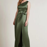 A studio photo of a brunette white woman wearing a body-hugging emerald green satin dress.