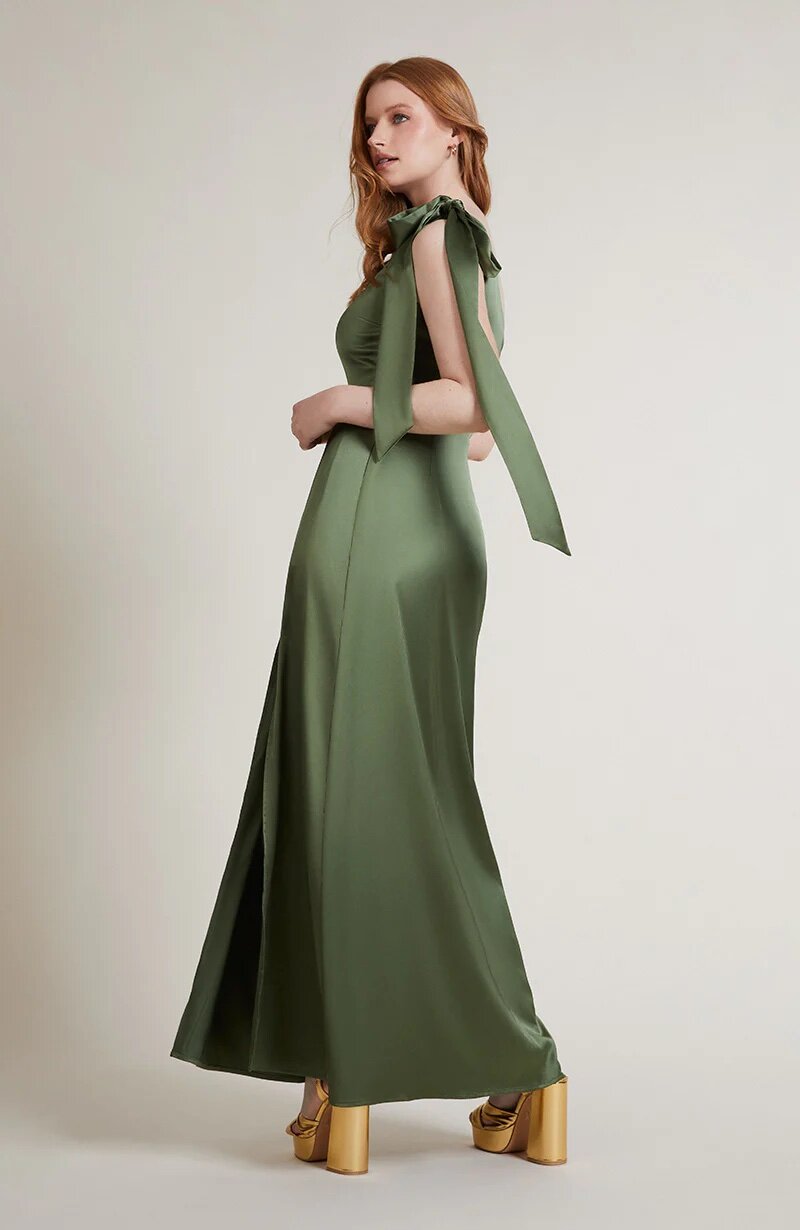 A studio photo of a brunette white woman wearing a body-hugging emerald green satin dress.