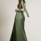 A studio photo of a brunette white woman wearing a body-hugging emerald green satin dress.
