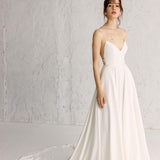 A woman wearing a white full gown with spaghetti straps, hand-appliquéd embroidery, and a cinched waist.