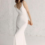 Model wearing a white Amalfi gown with a square heart neckline and a fluid bias cut skirt, and an open back with fabric-covered button detail.