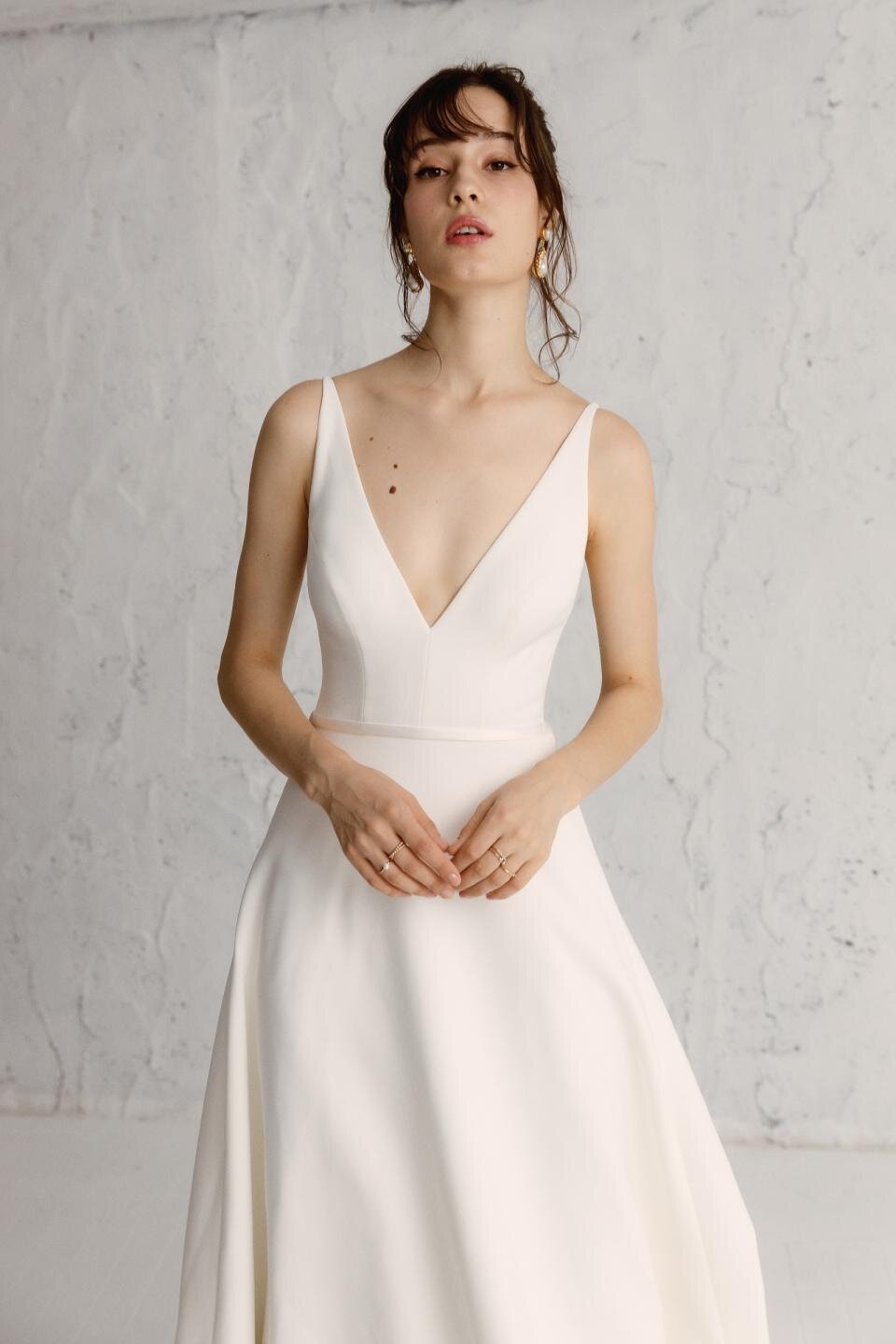 A woman wearing a white A-line Kaizen gown with a V-neckline and spaghetti straps.