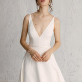 A woman wearing a white A-line Kaizen gown with a V-neckline and spaghetti straps.