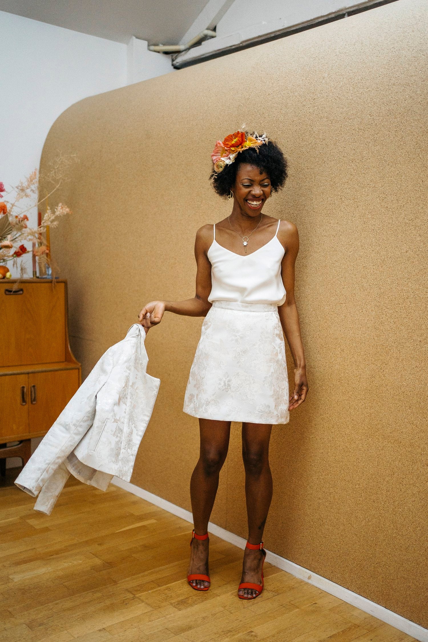 A woman wearing a white satin camisole top with a floral headband and holding a white jacket.
