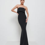 A woman wearing a black, floor-length, sleeveless maxi dress with a v-neckline.