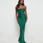 A woman wearing an emerald green maxi dress with a cowl neckline and spaghetti straps, made from a luxurious satin fabric.