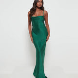 A woman wearing an emerald green maxi dress with a cowl neckline and spaghetti straps, made from a luxurious satin fabric.