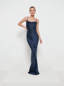 A woman wearing a navy maxi dress with a cowl neckline and spaghetti straps.