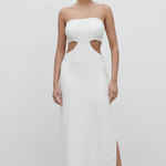 A woman wearing a white maxi dress with a bandeau neckline, cut-out designs, and a side slit. She is posing against a plain background.